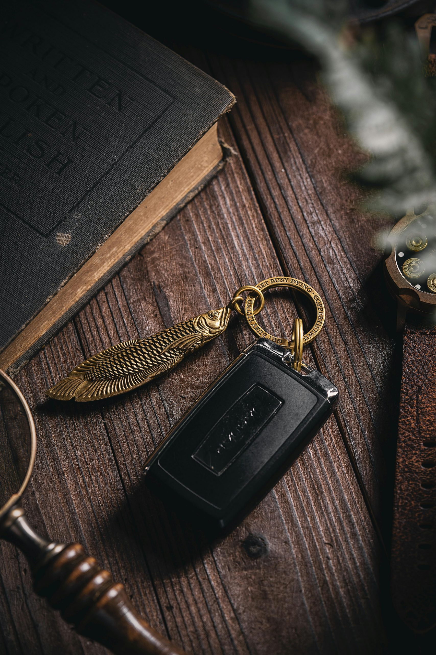 Home Close-up of a fish-shaped brass keychain next to a vintage book on a wooden table.