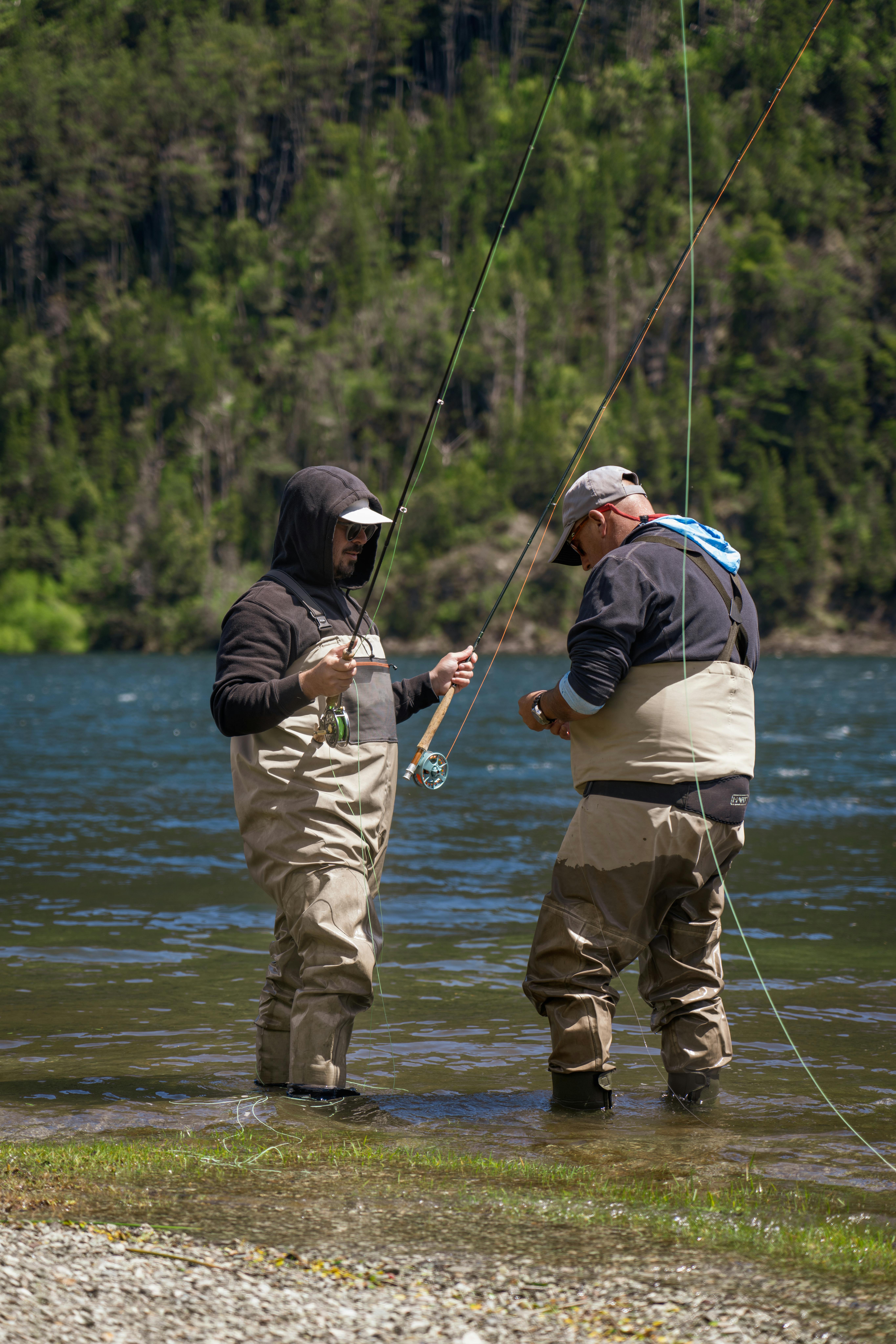 Home Two men fly fishing in a scenic Patagonian lake, surrounded by lush forests.