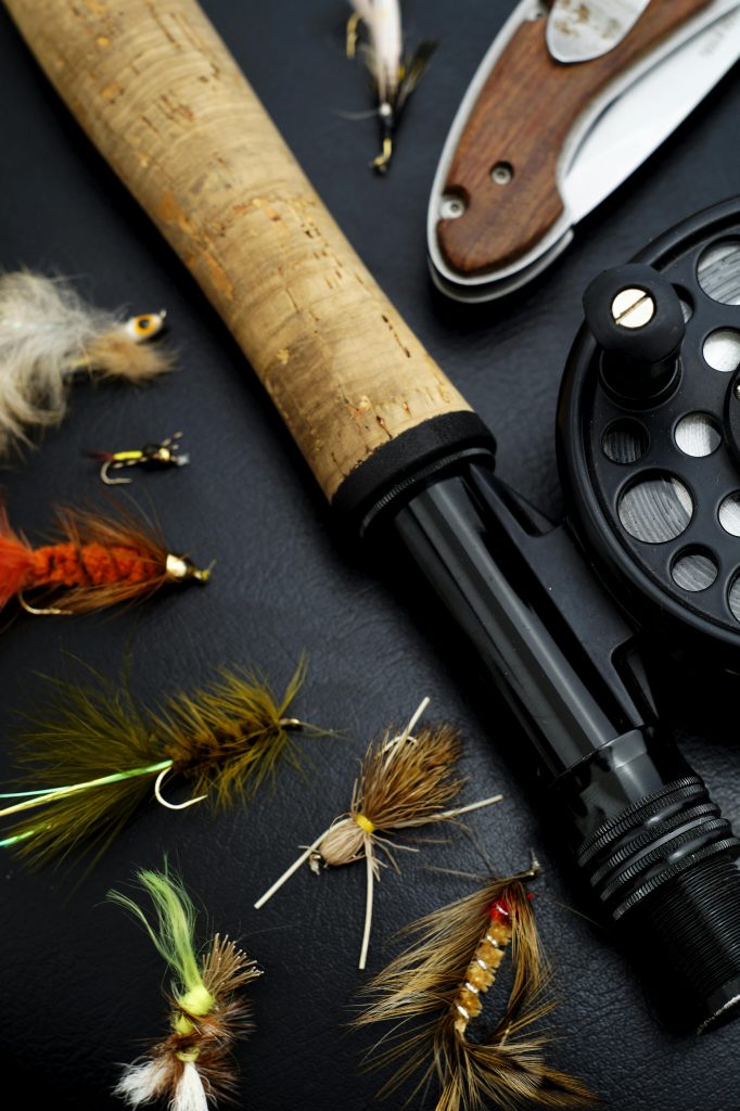 Home Detailed view of fly fishing gear including rod, reel, and colorful flies on a dark surface.